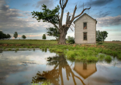 A photo of a dilapidated house next to a pond with a cloudy sky.