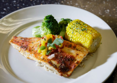 A photograph of fish, corn, and broccoli.
