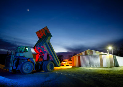 A photo of a dump truck at dusk illuminated with colored hues.