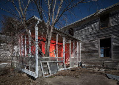 A nocturnal photo of a dilapidated home illuminated with red light.