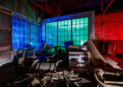 A photo of a deserted warehouse with large windows illuminated by colored hues.