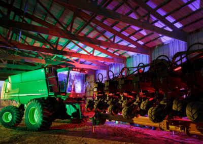 A nighttime photo of a farm combine illuminated with colored hues.