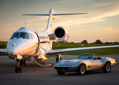 A photograph of a sunset at the airport with a jet and Corvette.