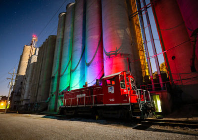 A photo of grain elevators at night lit up with red, green, and blue hues.