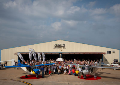 A photograph of the attendees in front of a hangar with several airplanes.