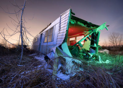 A photo of a abandoned mobile home lit with red, blue, and green hues.
