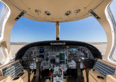 A wide-angle photograph of a jet cockpit interior with yokes, fight instruments and windows.