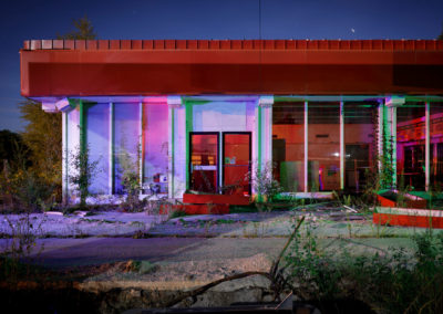 A photograph of the facade of an dilapidated filling station lit with red, green, and blue colors.
