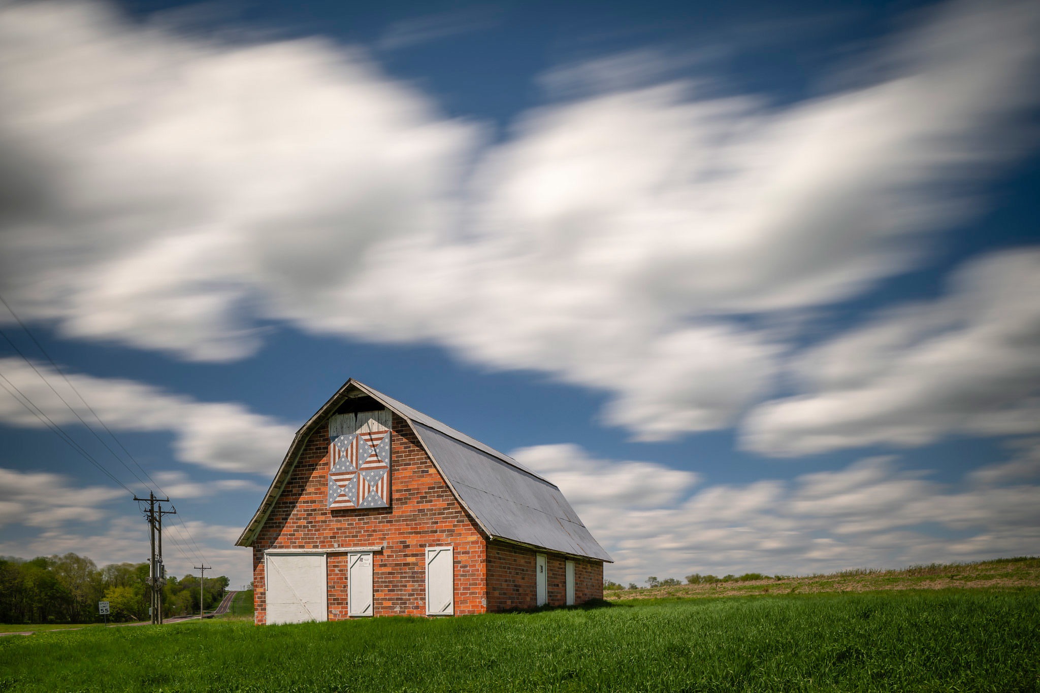 A photograph of a quilt motif on a barn with moving clouds above.